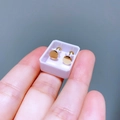 Nahaufnahme kleiner runder goldener Ohrstecker mit Schraubverschluss zwischen Fingern - Rund