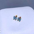 Makroaufnahme der Schmetterlings-Ohrstecker mit hellblauem Emaille und lila Edelstein - Blauer Emaille-Schleifenstil / Blaue Schleife