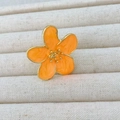 Macro view of bright orange camellia ring with gold trim in a beige jewelry tray - Orange