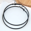 Detailed view of large black matte hoop earrings with a secure clasp on a white surface - Black