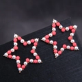 Boucles d'oreilles étoiles dorées avec perles blanches et corail sur boîte à bijoux - Rose