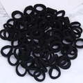 Detail of bulk black ribbed elastic hair ties stacked on white marble background - Black