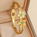Detail view of gold clover spring bangle with green gemstones on champagne jewelry box - Double Flower Design / Gold