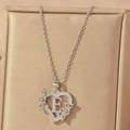 Detail of silver heart pendant with letter E, cubic zirconia, and green floral accents - Hollow Heart Letter E Necklace / Silver