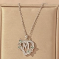 Macro detail of silver heart necklace with letter M and green floral accents - Hollow Heart Letter M Necklace / Silver