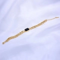 Detalle de una pulsera dorada con gema negra rectangular y cadena de eslabones cubanos - Pulsera / Negro