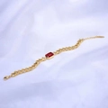 Detalle de collar de cadena dorada con colgante de rubí rectangular sobre seda blanca suave - Pulsera / Rojo