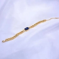 Detalle de una pulsera de cadena dorada con un cristal azul de corte rectangular - Pulsera / Azul