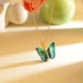 Teal gradient butterfly pendant necklace on a gold chain against a floral backdrop - Green Phantom Butterfly Gold