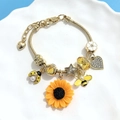 Detail of gold snake chain bracelet with sunflower, bee and heart charms on a ceramic plate - Gold Snake Bone Chain Style / Small