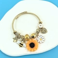 Gold charm bangle with sunflower, bee, daisy and heart pendants on stone tray - Gold Open Bangle Style