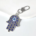 Silberner Hamsa-Hand Schlüsselanhänger mit blauem Auge und Strass auf weißem Sockel - Silber Blau Kristall Stil