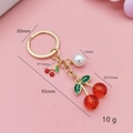 Detail of red cherry keychain with pearl pendant showing dimensions on pink background - Transparent Red Round Cherry
