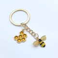 Porte-clés doré avec pendentifs abeille et alvéole, détails en émail jaune sur blanc - Style Abeille et Nid d'abeille