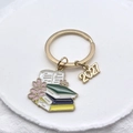 Gros plan du porte-clés doré de remise des diplômes avec pendentif livre et charme 2027 - Motif Livres Empilés Et Fleurs De Cerisier (2027)