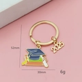 Détail d'un porte-clés de remise de diplôme 2025 avec chapeau bleu sur fond rose - Toque De Diplômé Bleu Foncé Et Livres Multi-couches (2025)