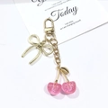 Détail d'un porte-clés cerise rose en résine pailletée avec nœud doré sur carte déco - Cerise (Fermoir en or KC) / Rose Pailleté
