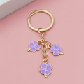 Porte-clés doré orné de trois trèfles violets élégants sur un fond rose pastel - Violet