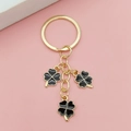 Porte-clés trèfle doré avec trois breloques en émail noir sur un fond rose poudré - Noir
