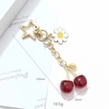 3D red cherry keychain with golden leaf and daisy charm on a white background - Red Cherry Daisy Star Hook