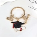 Porte-clés graduation 2026 doré avec breloques toque noire et diplôme en rouleau - Année de Diplôme et Style Mortier à Gland