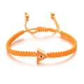 Macro detail of hand-woven orange cord bracelet with evil eye gold triangle charm - Orange