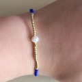 Detail of a white pearl bead with blue and gold beads on a stretchy elastic bracelet - Blue