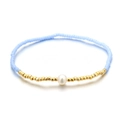 Pulsera elástica con cuentas azul claro, detalles dorados y una perla blanca central - Aguamarina