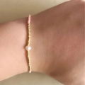 Pink and gold Miyuki bead bracelet with a central white pearl on a model's wrist - Pink