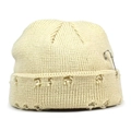 Detail of off-white knitted beanie featuring distressed holes and silver safety pin accessory - Beige