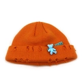 Close-up of bright orange knitted beanie with distressed rip details and blue bear charm - M / Orange