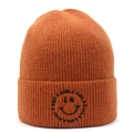 Close-up of ginger yellow knit beanie featuring black smile embroidery and ribbed texture - Caramel color