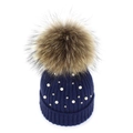 Detailed close-up of navy knit beanie featuring white pearls and a large fluffy fur pompom - Navy Blue