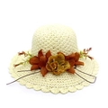 Detailed view of handwoven straw sun hat with decorative fabric flowers and wavy brim - Cream