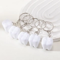Set of five white tooth-shaped keychains with silver metal rings on white textured background - White Keychain Collection