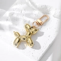Glossy golden balloon dog keychain with spring clip hook on textured white stone - Gold