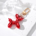 Vibrant red resin balloon dog keychain with polished gold hardware on a textured stone base - Red