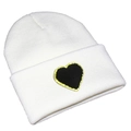 Close-up of white knit beanie featuring a black heart patch with gold sequin border - White