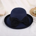 Detail of navy blue straw sun hat featuring a large black bow on a minimalist fabric background - Dark Blue