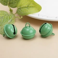 Trois cloches métalliques vertes laquées avec boucles de suspension sur fond beige clair - Vert