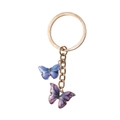 Dettaglio di portachiavi dorato con ciondoli a farfalla smaltati in blu e rosa vivace - Stile Doppia Farfalla / Viola