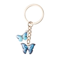 Dettaglio portachiavi dorato con ciondoli a farfalla blu sfumata e bordi metallici fini - Stile Doppia Farfalla / Blu