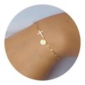 Detailweergave van een gouden kruisarmband met een ronde letter I bedel om de pols - Letter C