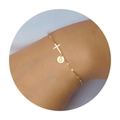 Detailopname van een gouden kruisarmband met een ronde letter O hanger om de pols - Letter D
