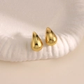 Vista macro de pendientes de gota dorados con acabado de espejo pulido en un plato blanco - Estilo Gota de Agua Brillante Simple (EH231)