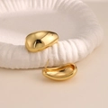 Vista detallada de pendientes dorados con forma de gota de agua y acabado de espejo pulido - Estilo Gota de Agua Aerodinámica Minimalista (EH230)