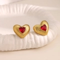 Detalle de pendientes de corazón dorados con gema roja y textura metálica plisada - Estilo Gema Corazón Rojo (EH225)