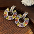 Macro view of C-shaped drop earrings featuring colorful oval zircons on a dark wood tray - Silver - Rainbow
