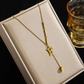 Goldene Titanstahl-Halskette mit F-Anhänger und Würfelquaste auf einer Schmuckschatulle - Buchstabe F
