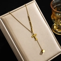Goldene Titanstahl-Halskette mit T-Anhänger und Würfel auf Schmuckschatulle präsentiert - Buchstabe T
